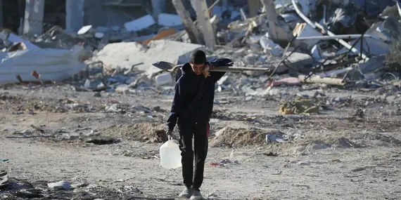 A Palestinian youth walks through the ruins of homes in Rafah, southern Gaza Strip, carrying a water jerrican and a shovel. Photo: UNICEF//UNI724700/El Baba