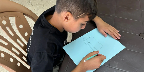 Kareem drawing a fire truck, sharing his dream of becoming a fireman. Three months ago, limited by his injury, he wished to be a carpenter. With nearly 90% recovery, his hopes have shifted back to firefighting, reflecting his progress and renewed sense of hope. Photo by © EJYMCA/Maha Sabbah