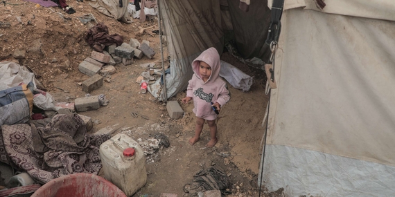A toddler stands amid debris and personal belongings outside a tent in the Gaza Strip. Photo by UNICEF.