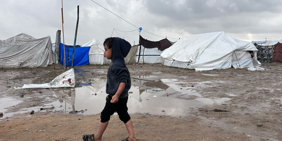 A Palestinian boy walks past tents during a break in the rain in Jabalya, North Gaza. Photo by OCHA