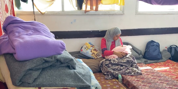 أم فلسطينية ورضيعتها في مدرسة تستخدم كمركز لإيواء المهجرين في قطاع غزة. تقول: «ليس ثمة حمام ولا مياه ولا رعاية مناسبة. ولم أفحص قطب العملية القيصرية ولم أنظفها بعد.» لقطة من فيديو أنتجته اليونيسف.