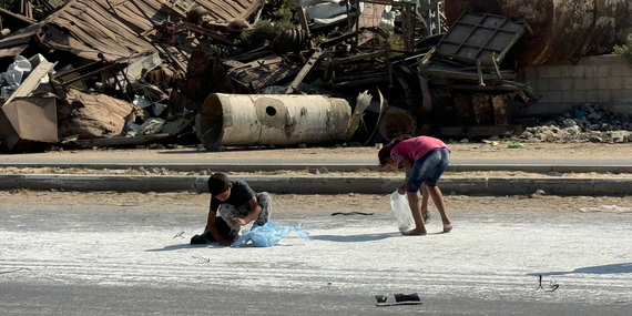 طفلان حافيي القدمين يجمعان الدقيق المتناثر من إحدى شاحنات المساعدات الإنسانية على طريق صلاح الدين في دير البلح بغزة وسط مخلّفات الحرب، 5 تشرين الثاني/نوفمبر 2024. تصوير مكتب الأمم المتحدة لتنسيق الشؤون الإنسانية