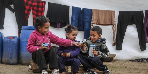أطفال يجلسون خارج خيمتهم في غزة، ويتقاسمون البسكويت الذي قدمه برنامج الأغذية العالمي. يملأ مئات الآلاف من المُهجّرين الآن شوارع جنوب غزة، ويعيشون في مراكز إيواء مؤقتة في ظروف بائسة، مع إمكانية ضئيلة للحصول على الغذاء والماء والأدوية والمأوى المناسب. تصور برنامج الأغذية العالمي/علي جادالله، كانون الثاني/يناير 2024