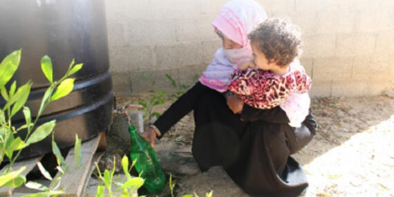 Mona filling a bottle of non-potable water from a tank in her yard. © Photo by OXFAM