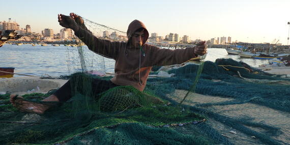Palestinian boy handling a fishing net in Gaza harbour, December 2015. Photo by OCHA