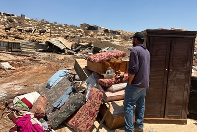 A Palestinian man next to some of his belongings, out in the open, following the demolition of 20 homes and other structures in Al Mughayyir. Photo by OCHA